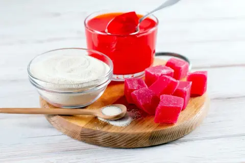 Agar, czyli substancja żelująca, w proszku i w postaci czerwonych kostek. Obok szklanka galaretki.
