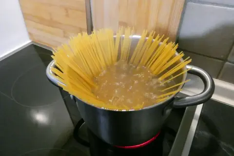 Długi makaron spaghetti gotuje się w garnku na płycie indukcyjnej. To pierwszy krok, jak ugotować makaron.