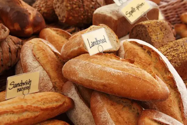 Różnorodne pieczywo, w tym bochenki z etykietami "Landbrood" i "Sandwich naturel". Zastanawiasz się, czym smarować chleb przed pieczeniem, by uzyskać chrupiącą skórkę?